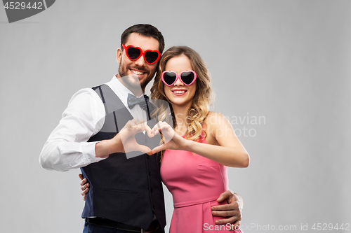 Image of couple in sunglasses making hand heart gesture