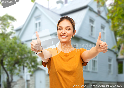 Image of teenage girl showing thumbs up over house