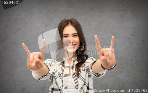 Image of teenage girl showing rock sign over concrete wall