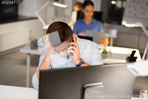 Image of stressed man calling on smartphone at night office