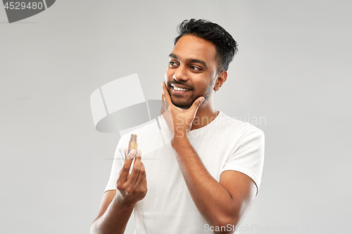 Image of smiling indian man applying grooming oil to beard
