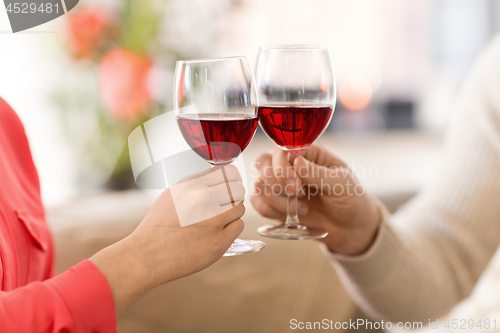 Image of hands of couple clinking red wine glasses