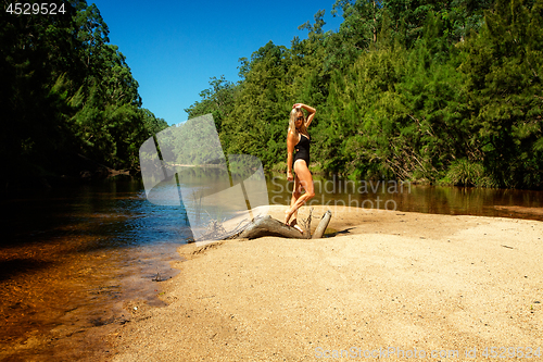 Image of Woman in swimsuit tanding on gnarled log on sand bar