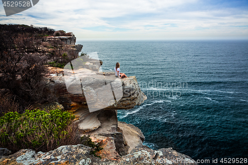 Image of Relaxed woman sitting on coastal headland looking out to ocean