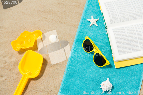 Image of sunglasses, sand toys and book on beach towel