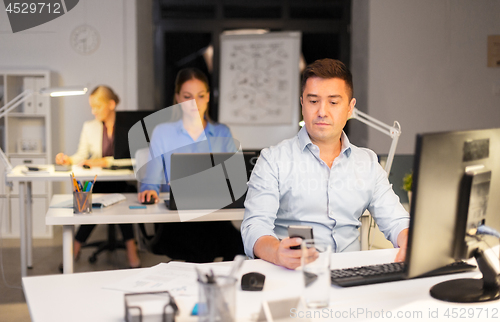 Image of man with smartphone working at night office