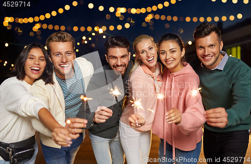 Image of happy friends with sparklers at rooftop party