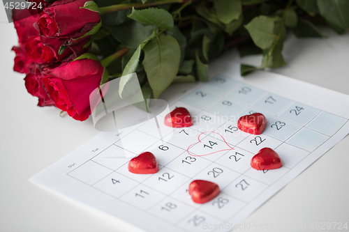 Image of close up of calendar, heart, candies and red roses