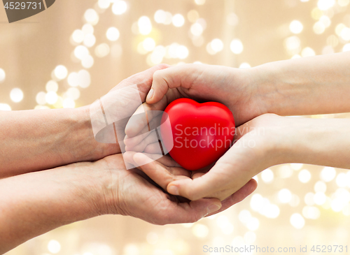 Image of senior and young man hands holding red heart