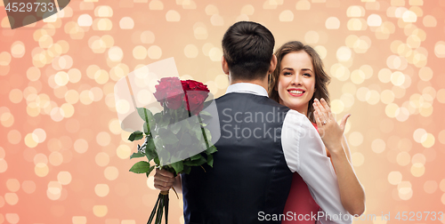 Image of woman with engagement ring and roses hugging man