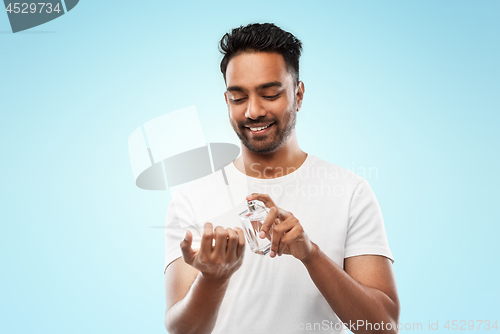 Image of happy indian man with perfume over blue background