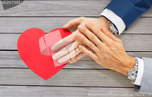 Image of close up of male gay couple hands with red heart