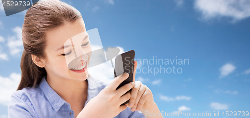 Image of smiling girl messaging on smartphone over blue sky