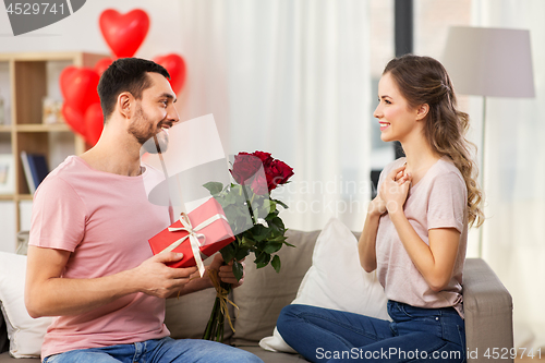 Image of happy man giving woman flowers and present at home