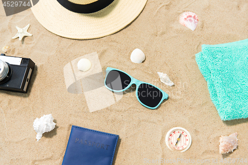 Image of camera, passport, sunglasses and hat on beach sand