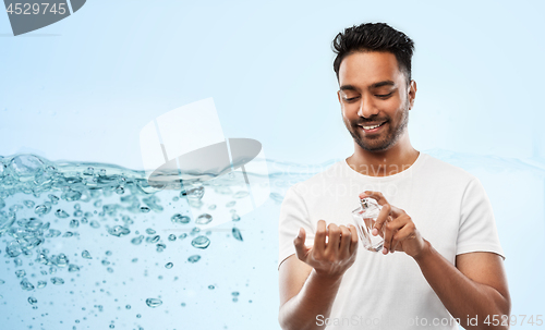 Image of happy indian man with perfume over blue background