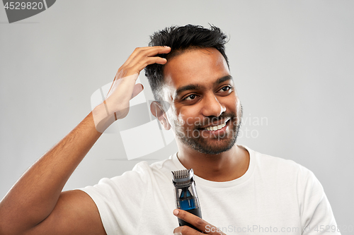 Image of smiling indian man with trimmer touching his hair