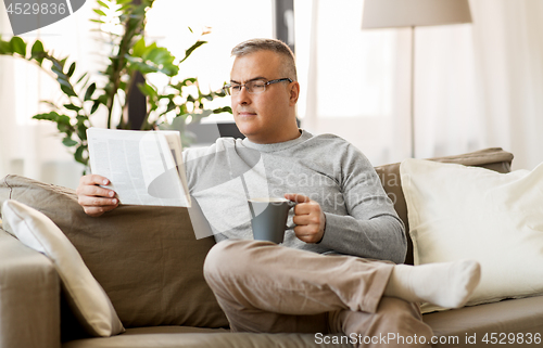 Image of man reading newspaper and drinking coffee at home