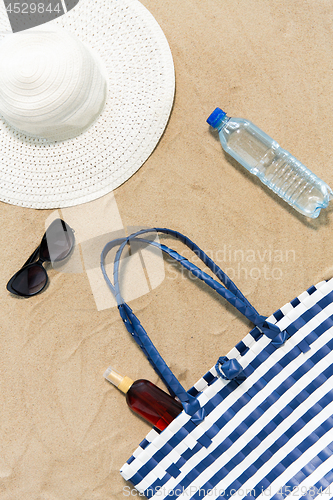 Image of beach bag, sunscreen, sunglasses and hat on sand