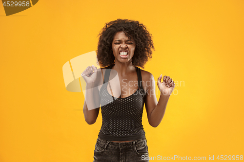 Image of Portrait of an angry woman looking at camera isolated on a gold background