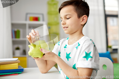 Image of little boy putting coin into piggy bank at home