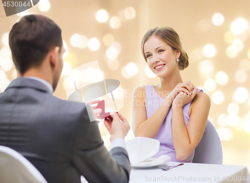 Image of man giving woman engagement ring at restaurant