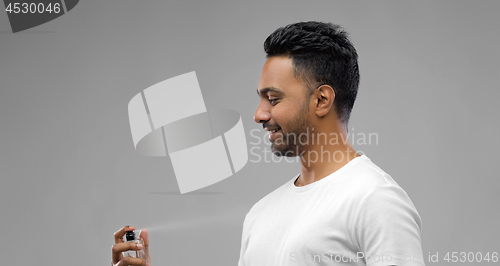Image of happy indian man with perfume over grey background