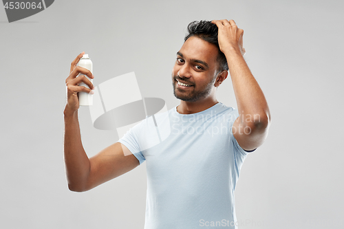 Image of smiling indian man applying hair spray over gray