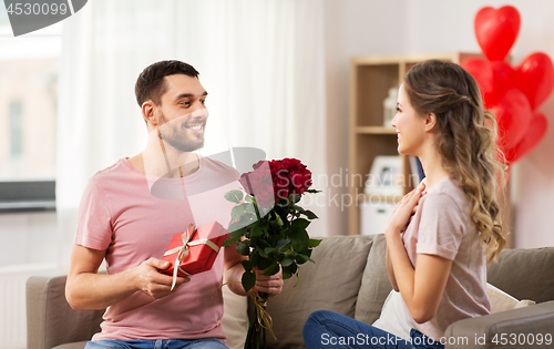 Image of happy man giving woman flowers and present at home