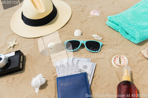 Image of money in passport, shades and hat on beach sand