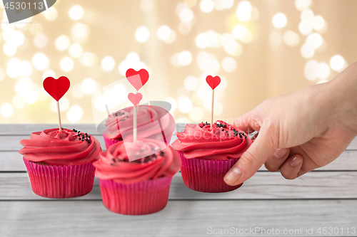 Image of close up of hand taking cupcakes with heart sticks