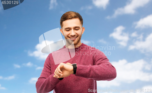 Image of smiling young man checking time on wristwatch