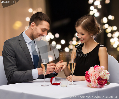 Image of man giving woman engagement ring at restaurant