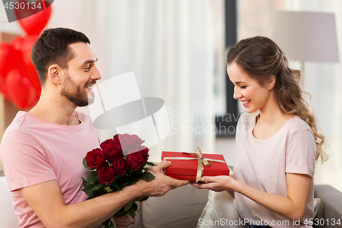 Image of happy man giving woman flowers and present at home