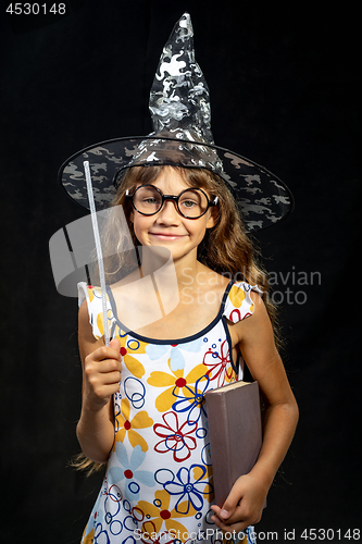 Image of Girl sorceress, with a book and a magic wand, in a hat, on a black background