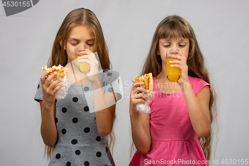 Image of Two girls drink juice and eat a bun