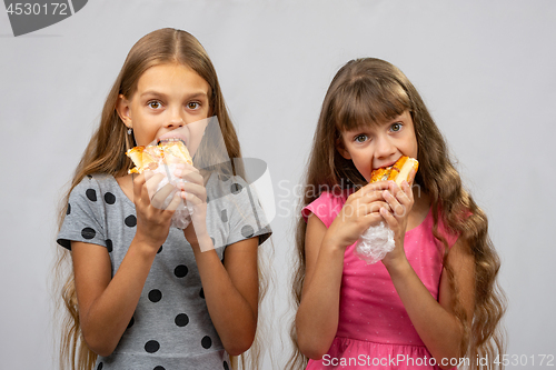 Image of Two hungry girls eat bread, and look at the frame