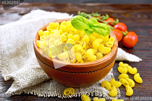 Image of Elbow macaroni in bowl with tomatoes and basil on board