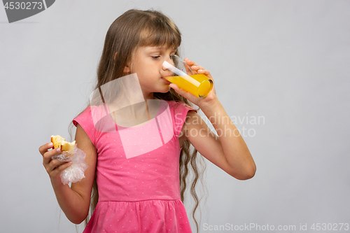 Image of A girl drinks orange juice and eats a bun