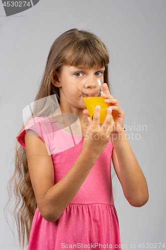 Image of The girl drinks orange juice from a glass and looks at the frame