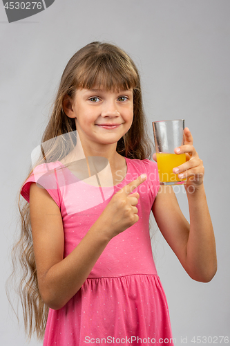 Image of A girl holds a glass of orange juice in her hand and points her finger at it