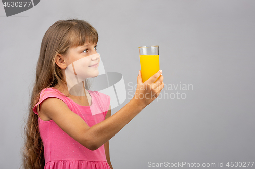 Image of A girl holds a glass of juice in her hand and looks at the empty space on the right