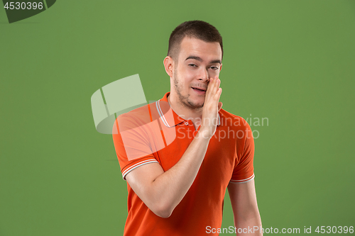 Image of The young man whispering a secret behind her hand over green background