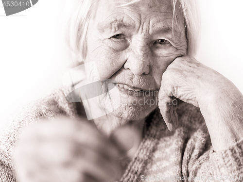 Image of Sad elderly woman sitting at the table at home and looking miserably at only remaining coin from pension in her hand.