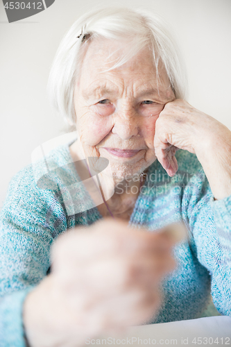 Image of Sad elderly woman sitting at the table at home and looking miserably at only remaining coin from pension in her hand.