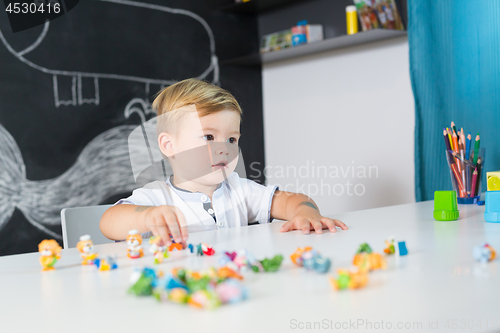 Image of Portrait of cute toddler boy playing with toys at the desk at home.