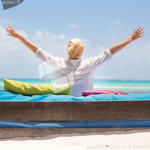 Image of Relaxed woman in luxury lounger, arms rised, enjoying summer vacations on beautiful beach.