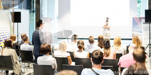 Image of Businessman in audience standing and asking question to speeker at business conference.