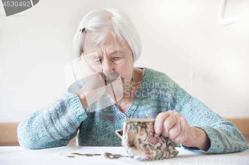 Image of Concerned elderly woman sitting at the table counting money in her wallet.