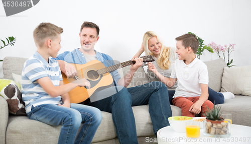 Image of Happy caucasian family smiling, playing guitar and singing songs together at cosy modern home